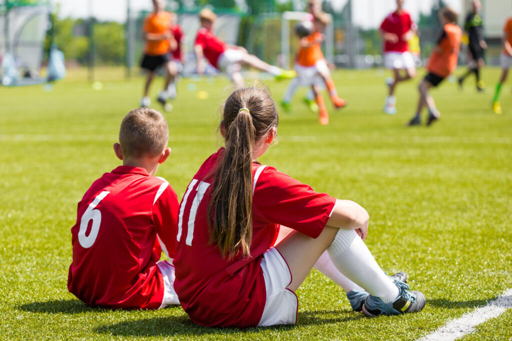 Children soccer players playing game. Young girl and boy soccer players sitting together on grass football field